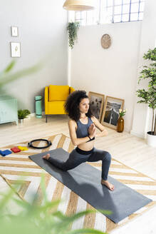 Woman in sports clothing doing sun salutation in living room - GIOF12147