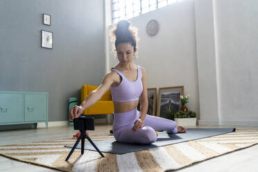 Weibliche Influencerin berührt ihr Smartphone, während sie zu Hause Yoga macht - GIOF12182
