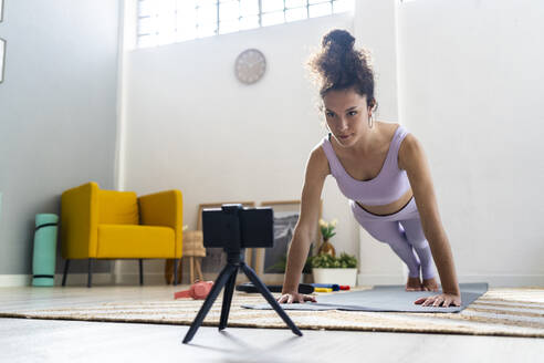 Female influencer doing push-ups while filming through mobile phone at home - GIOF12186