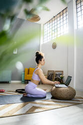 Female vlogger using laptop while kneeling at home - GIOF12196