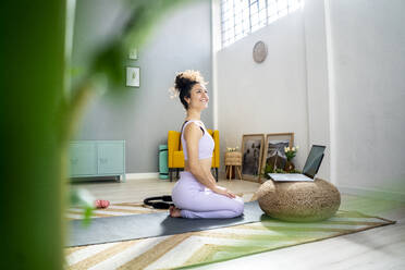 Smiling woman day dreaming while kneeling in front of laptop at home - GIOF12197