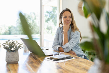 Blond hair entrepreneur sitting with laptop at table while looking away - SBOF03700
