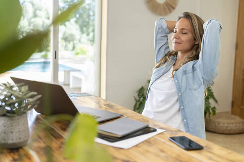 Female professional with hands behind head relaxing while siting at table - SBOF03703