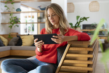 Frau benutzt digitales Tablet, während sie auf der Couch im Wohnzimmer sitzt - SBOF03709
