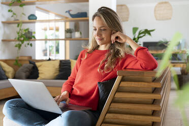 Woman using laptop sitting in living room at home - SBOF03712