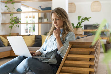 Mid adult woman using laptop in living room at home - SBOF03715