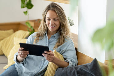 Smiling woman using digital tablet while sitting on couch in living room at home - SBOF03726