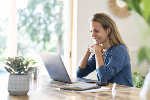 Lächelnde Unternehmerin, die am Tisch sitzend einen Laptop betrachtet - SBOF03739