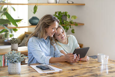 Mother and daughter sharing digital tablet while sitting at table - SBOF03748