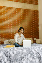 Frau benutzt Laptop, während sie zu Hause auf dem Bett sitzt - VABF04298