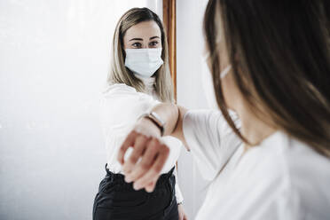 Female patient wearing protective face mask doing elbow bump with doctor at hospital - EBBF03223