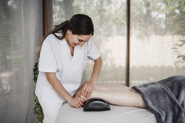 Smiling female physiotherapist massaging patient's foot in clinic - EBBF03252