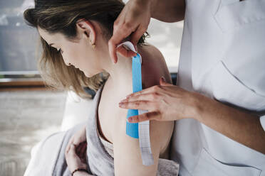 Therapeutin klebt elastisches therapeutisches Band auf die Schulter eines Patienten im Krankenhaus - EBBF03262