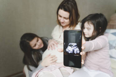 Neugierige Tochter mit Mobiltelefon zeigt Ultraschall-Embryo von Baby zu Hause - EYAF01567