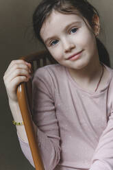 Smiling girl with blue eyes sitting on chair at home - EYAF01575