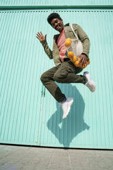 Fröhlicher Mann tanzt an einem sonnigen Tag vor einer türkisfarbenen Wand - AFVF08518