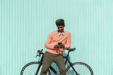 Mittelgroßer erwachsener Mann, der sich an ein Fahrrad lehnt, während er an einem sonnigen Tag sein Smartphone benutzt - AFVF08526