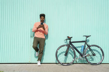 Handsome man standing by bicycle while using smart phone during sunny day - AFVF08528