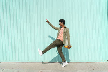 Mittlerer erwachsener Mann, der auf eine türkisfarbene Wand zeigt, während er an einem sonnigen Tag spazieren geht - AFVF08532