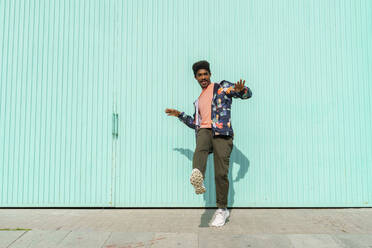 Mann tanzt vor einer türkisfarbenen Wand an einem sonnigen Tag - AFVF08535