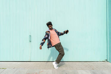 Ekstatischer Mann hält sein Smartphone und tanzt vor einer türkisfarbenen Wand - AFVF08539
