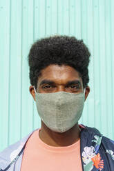 Mid adult man wearing protective face mask in front of turquoise wall - AFVF08540