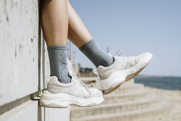 Mid adult woman dangling feet while sitting on retaining wall - AFVF08553