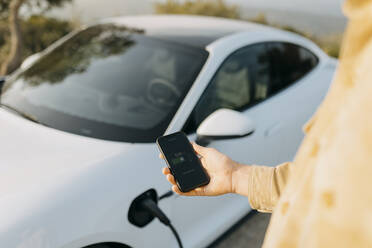 Man checking battery level of electric car on smart phone - GMCF00131