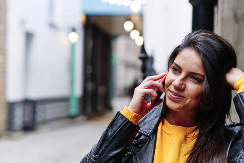 Lächelnde Frau, die in der Stadt mit einem Mobiltelefon spricht - ASGF00204