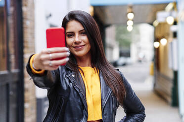 Lächelnde Frau nimmt Selfie durch Handy in der Stadt - ASGF00205