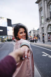 Happy woman holding hand of boyfriend on street in city - ASGF00219