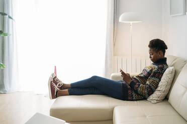 Junge Frau benutzt ihr Smartphone, während sie auf dem Sofa im Wohnzimmer sitzt - MPPF01610