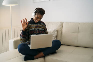 Smiling freelancer waving on video call through laptop in living room - MPPF01613
