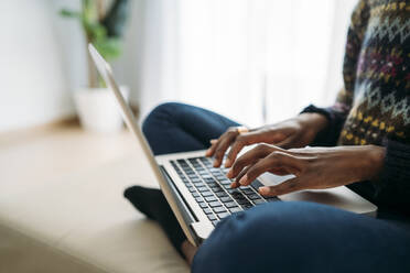 Weibliche Fachkraft tippt auf einem Laptop, während sie im Wohnzimmer zu Hause arbeitet - MPPF01614