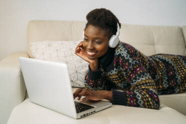 Lächelnde junge Geschäftsfrau, die einen Laptop benutzt und zu Hause Kopfhörer trägt - MPPF01618