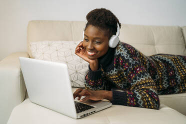 Smiling young businesswoman using laptop while wearing headphones at home - MPPF01618