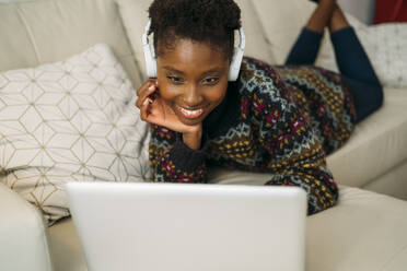 Smiling young female freelancer working on laptop while lying on front at home - MPPF01620