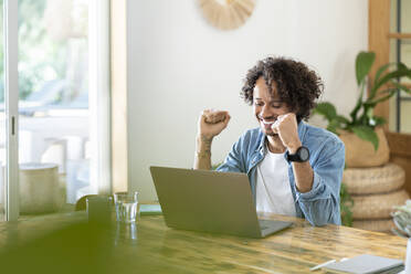 Ecstatic male professional celebrating success in front of laptop at home - SBOF03751