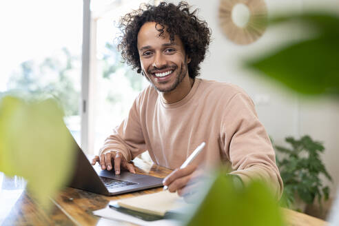 Male entrepreneur with laptop writing in diary on table at home - SBOF03767