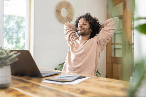 Male entrepreneur relaxing with hands behind head while laptop on table at home - SBOF03769