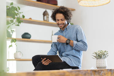 Smiling male professional using digital tablet while holding coffee cup at home - SBOF03781