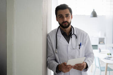 Männlicher Angestellter im Gesundheitswesen mit digitalem Tablet, das an der Wand lehnt - GIOF12207