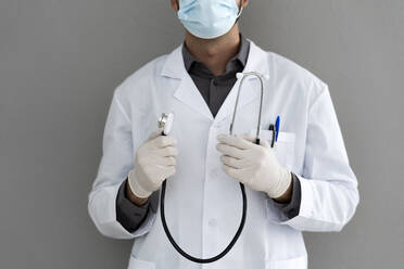 Male doctor wearing surgical glove holding stethoscope in front of wall - GIOF12209