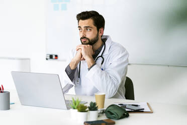 Male healthcare worker sitting with hand on chin while looking away - GIOF12222