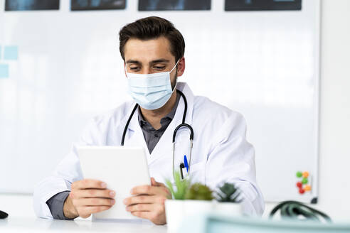 Männlicher Arzt mit Gesichtsschutzmaske bei der Arbeit mit einem digitalen Tablet im Krankenhaus - GIOF12227