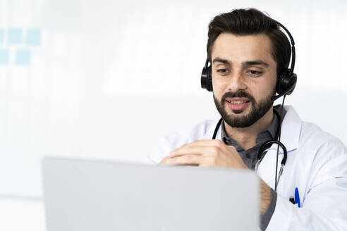 Ein männlicher Arzt trägt einen Kopfhörer, während er in einem Krankenhaus eine Videokonferenz abhält - GIOF12241