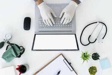 Männlicher Arzt mit chirurgischem Handschuh tippt auf einem Laptop - GIOF12265