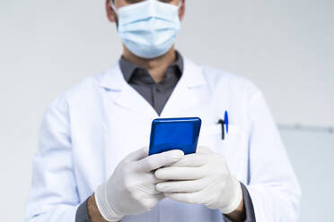 Male doctor text messaging through smart phone in hospital during COVID-19 - GIOF12268