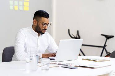 Männlicher Unternehmer mit Laptop auf dem Schreibtisch bei der Arbeit im Büro - GIOF12273