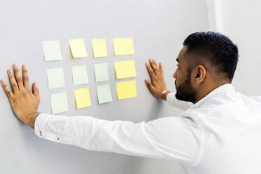 Male entrepreneur looking at business strategy on wall at office - GIOF12284